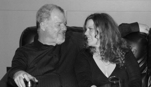 A black and white photo of a man and woman sitting on a couch and smiling at each other.