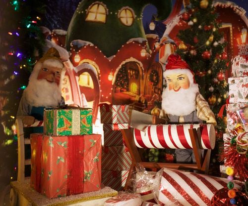 An animatronic elf saws a peppermint log and another pushes a cart full of wrapped presents.